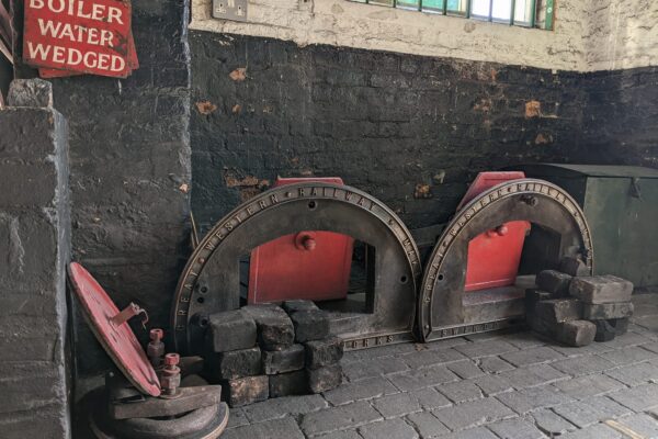 Black, grey and red metal work from front of Lancashire Boiler piled on grey stone floor.